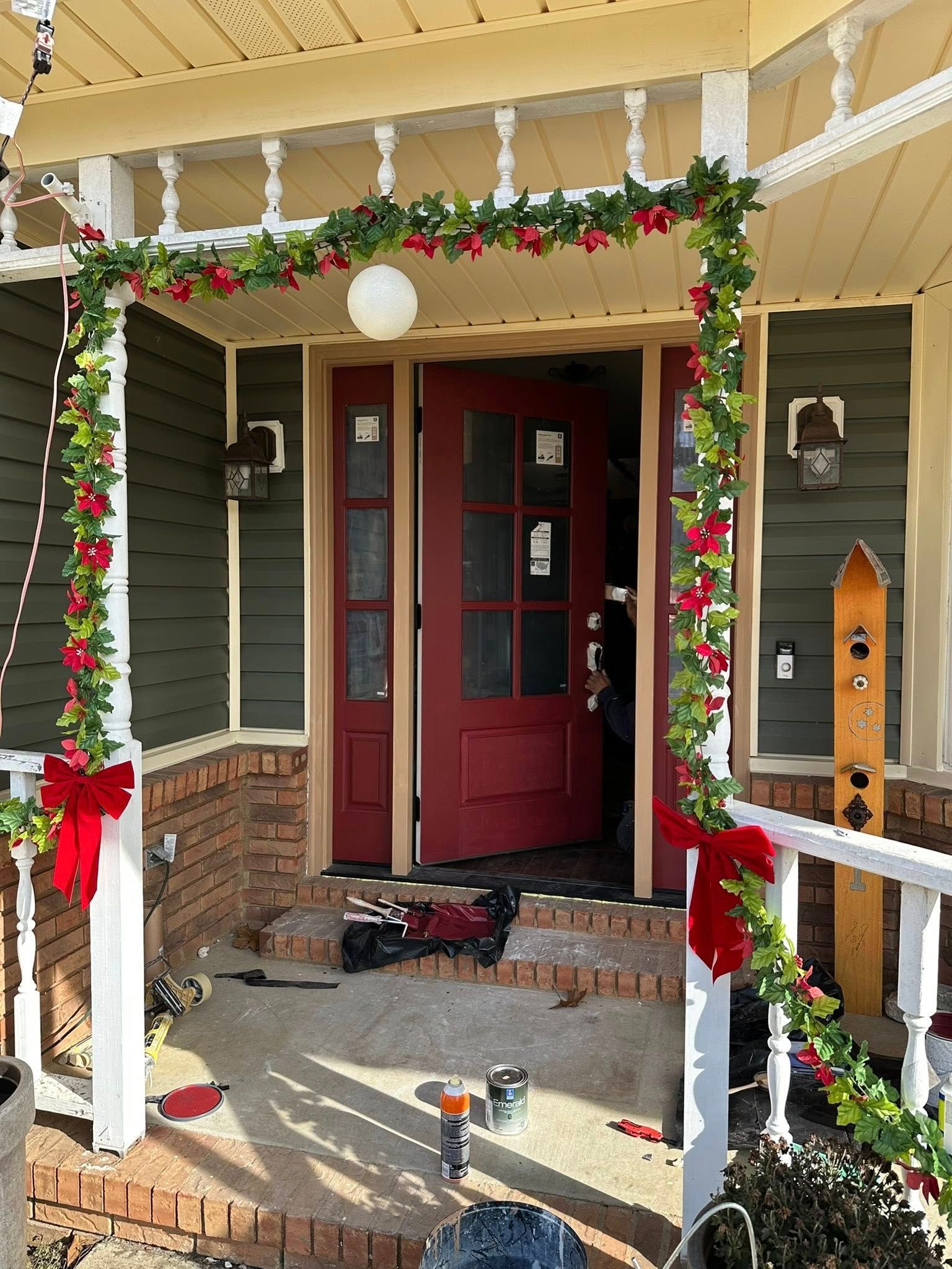 Front porch with red door, Christmas garland, and scattered shoes on the steps