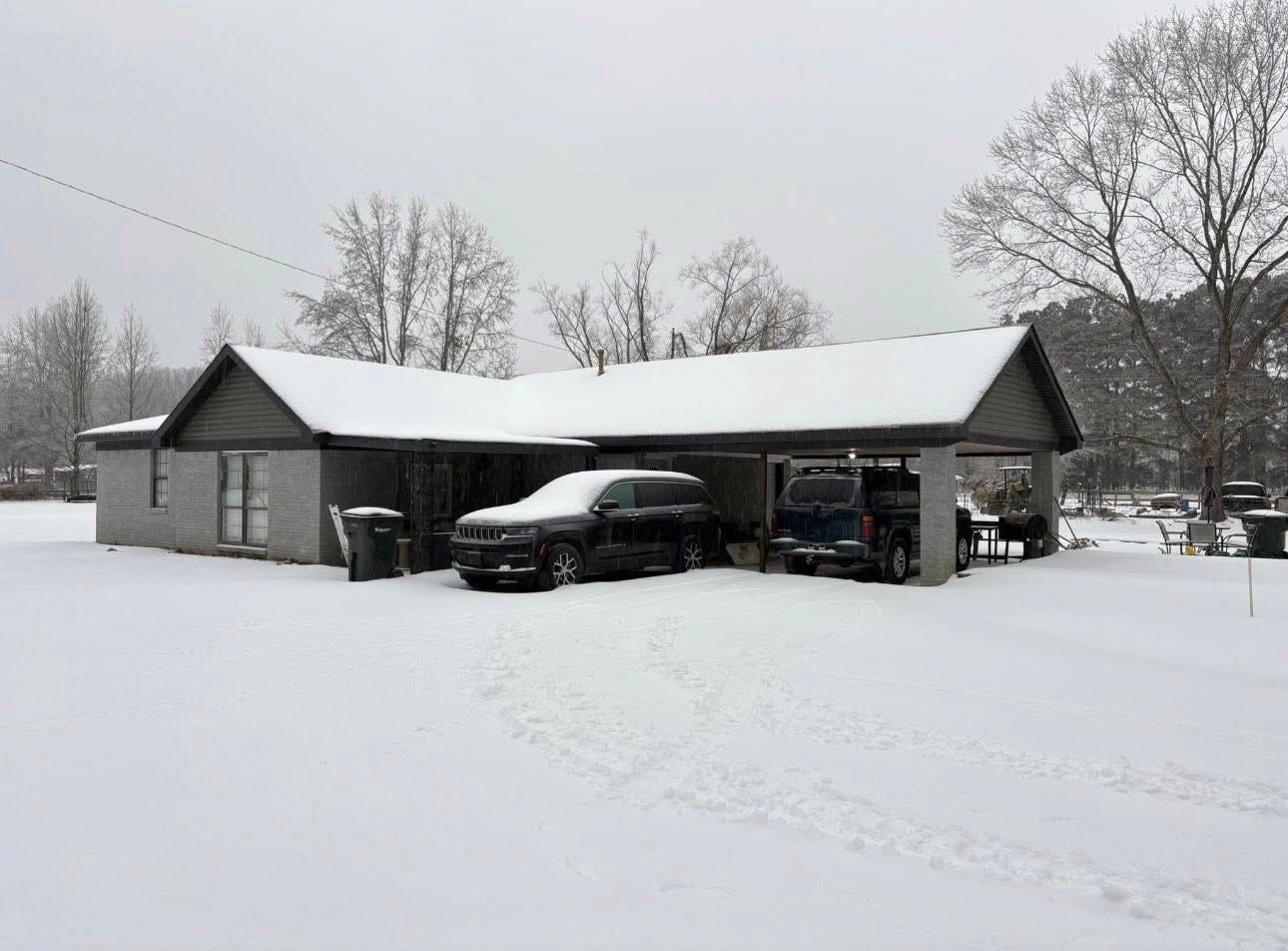 Snow-covered house with a car parked under the carport in a winter yard