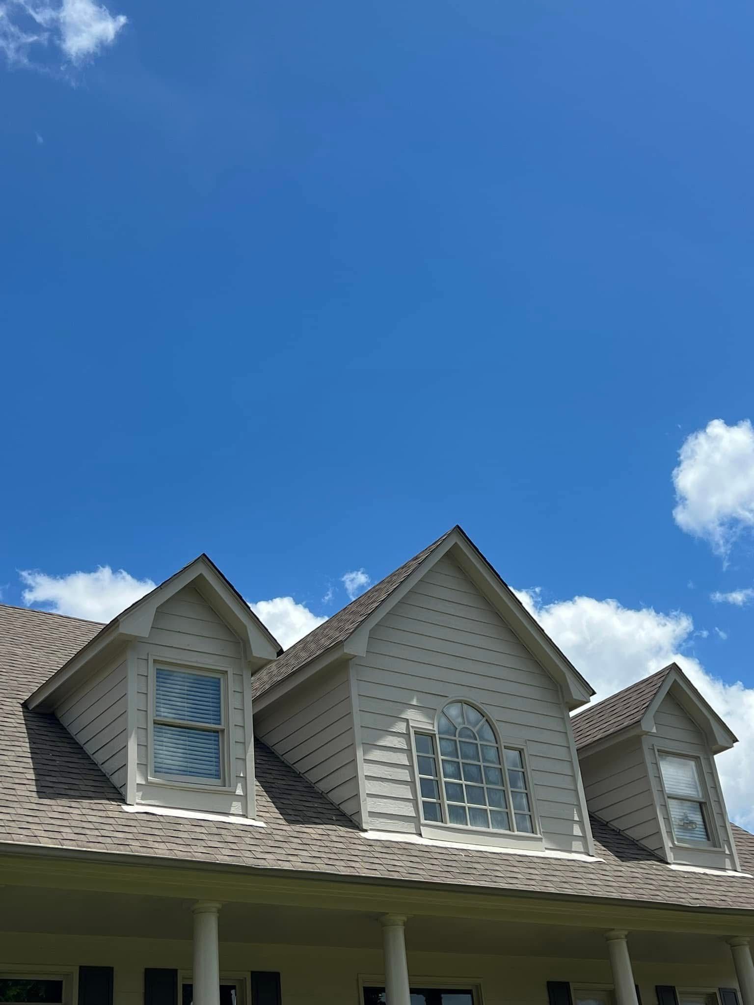 Suburban house roofline with dormer windows against a bright blue sky and small clouds