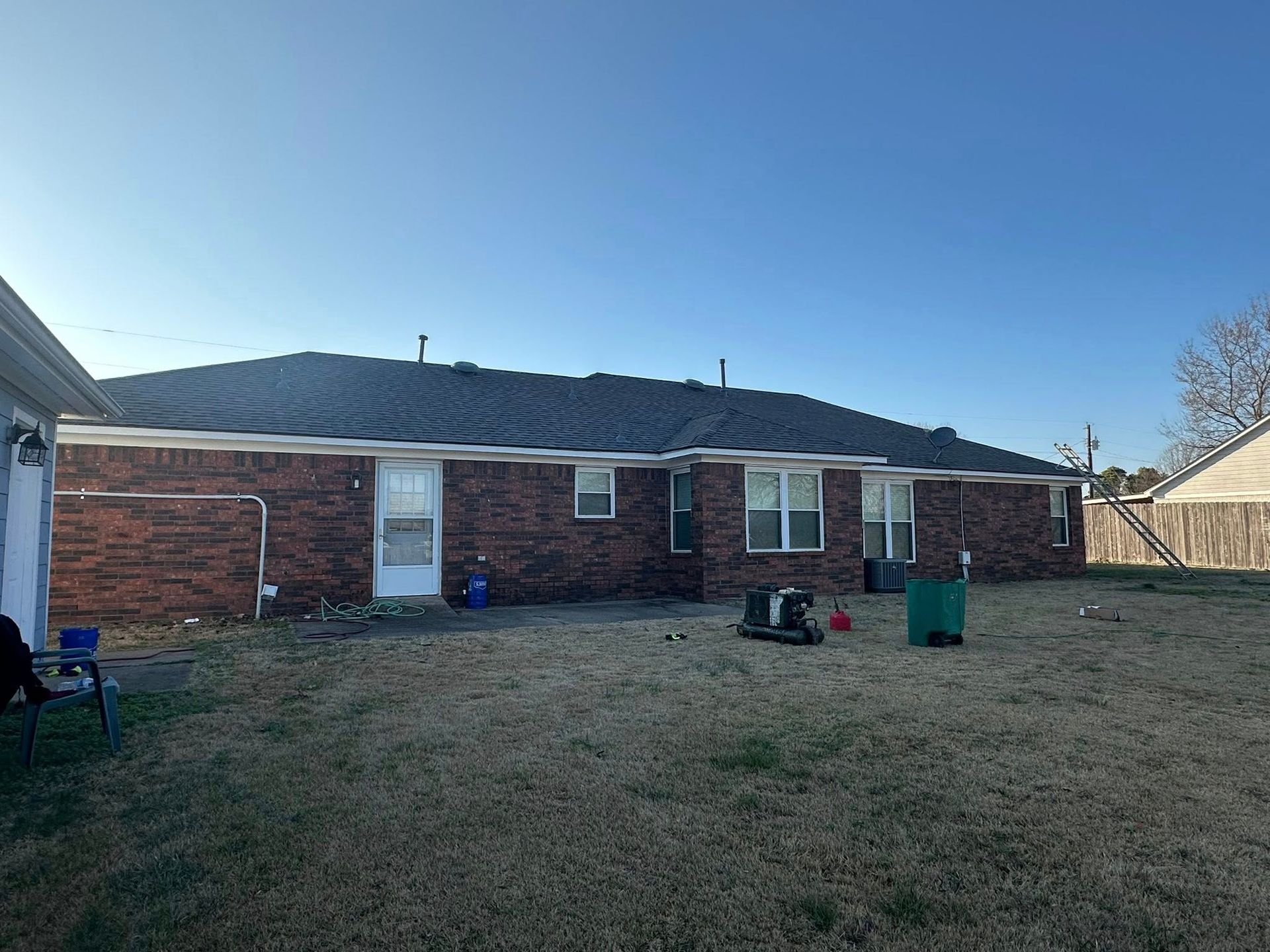 Backyard view of a single-story brick house with a dark roof and sparse winter grass
