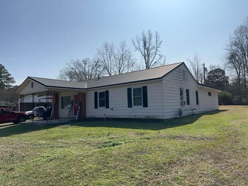 Single-story white house with black shutters, a carport, and a grassy yard on a sunny day