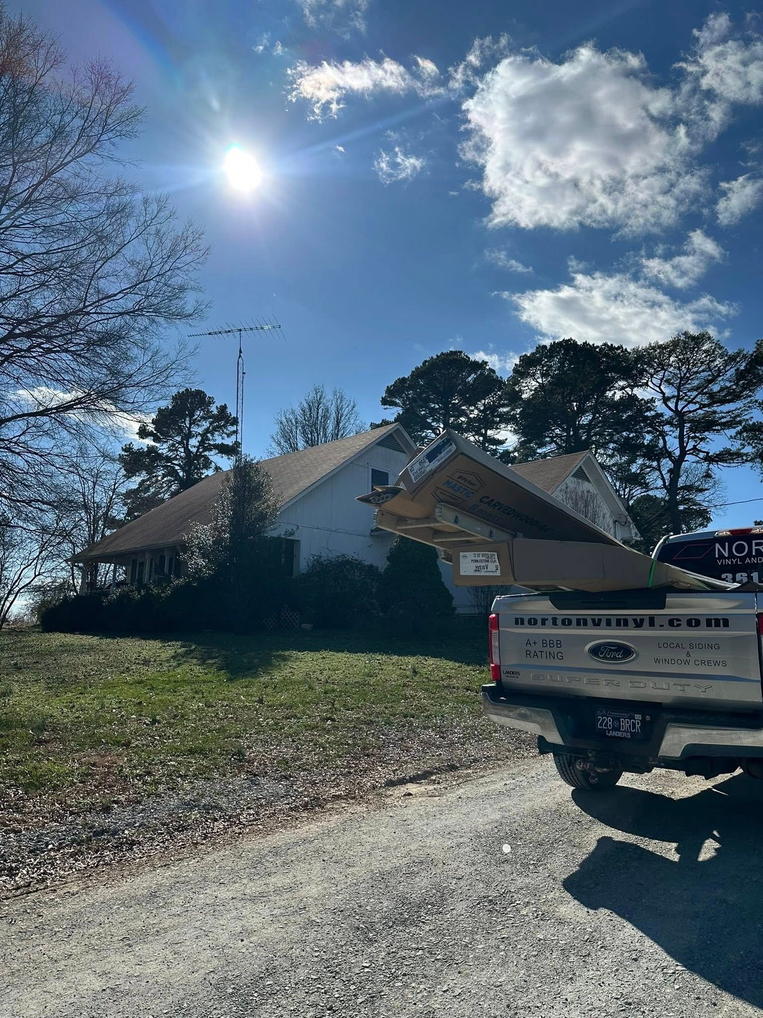 Sunny residential street with a white pickup truck, house, trees, and blue sky with clouds
