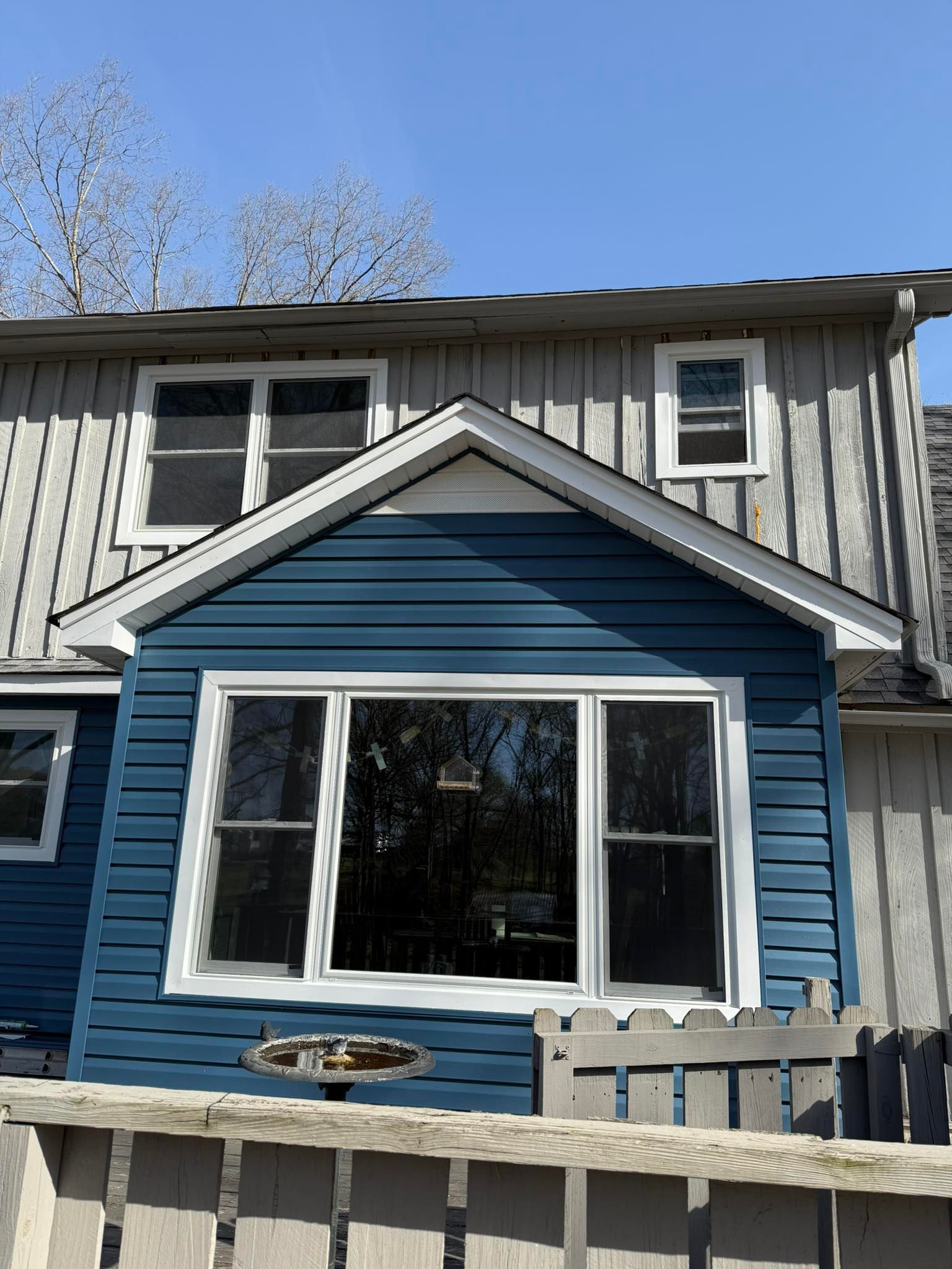 Blue and white house exterior with a large front window and fenced yard under a clear sky