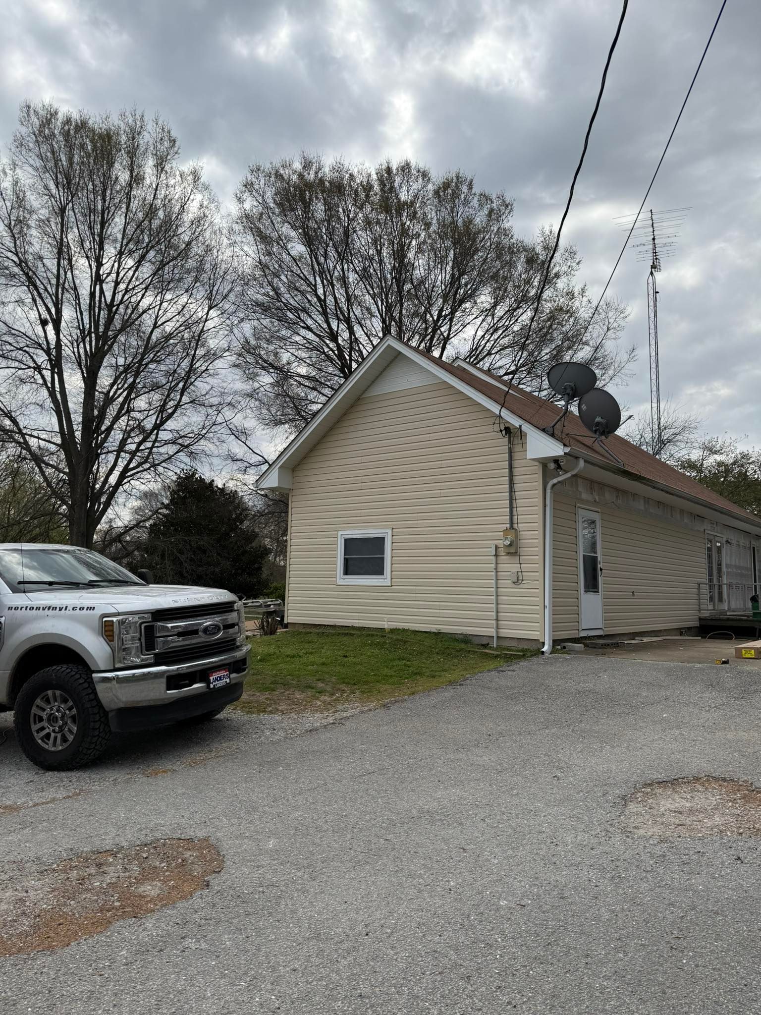 Small beige house with gravel driveway, parked pickup truck, and cloudy sky overhead