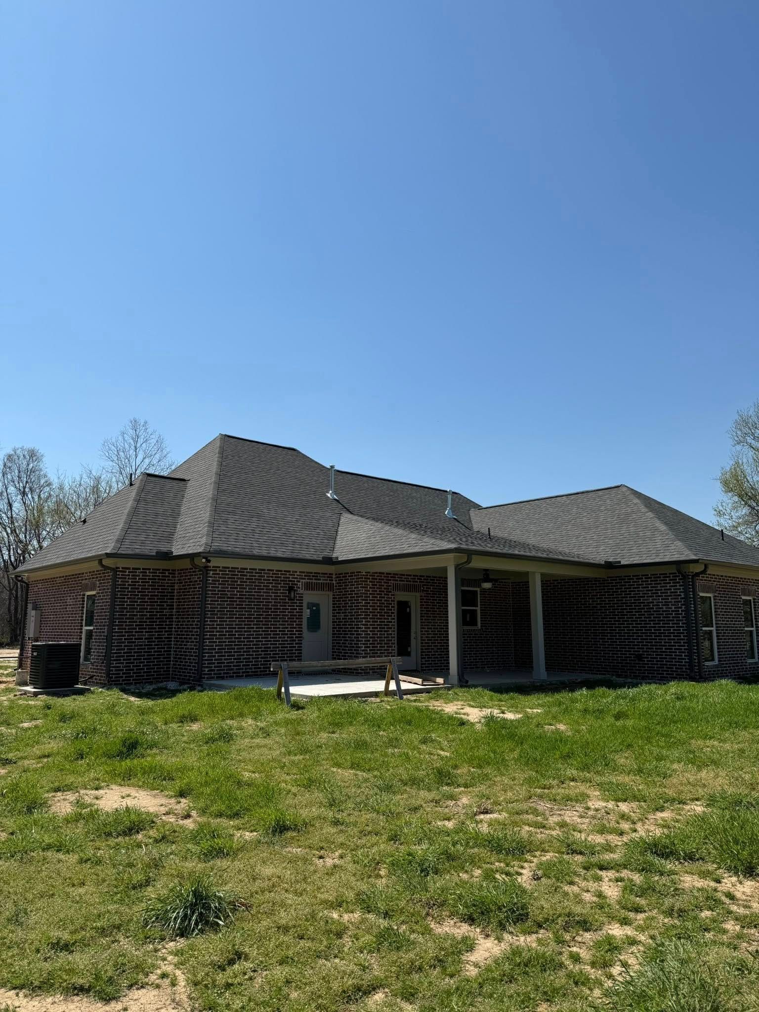 Single-story brick house with a dark roof on a grassy hill under a clear blue sky