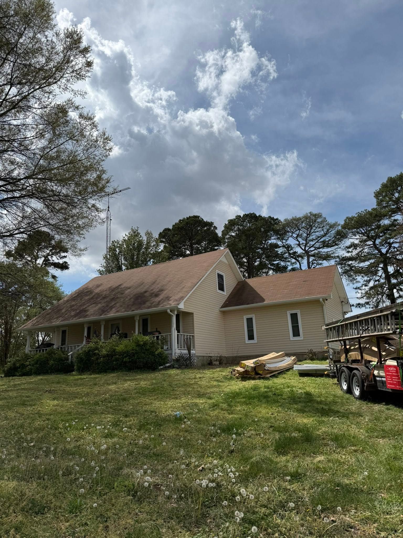 House with a steep roof on a grassy hillside under a cloudy sky, with trees and a trailer nearby