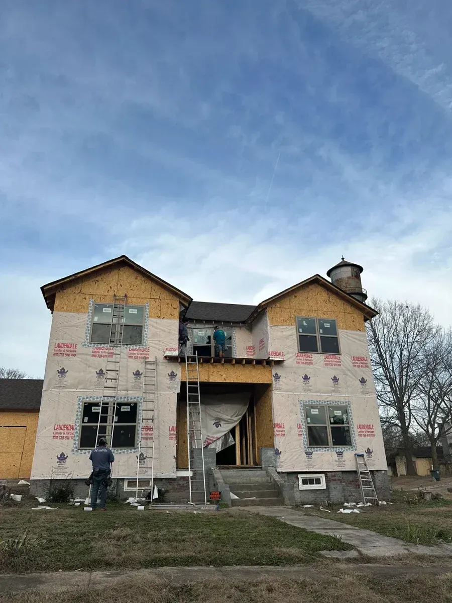 Two-story house under renovation with exposed siding, front stairs, and a partly cloudy sky