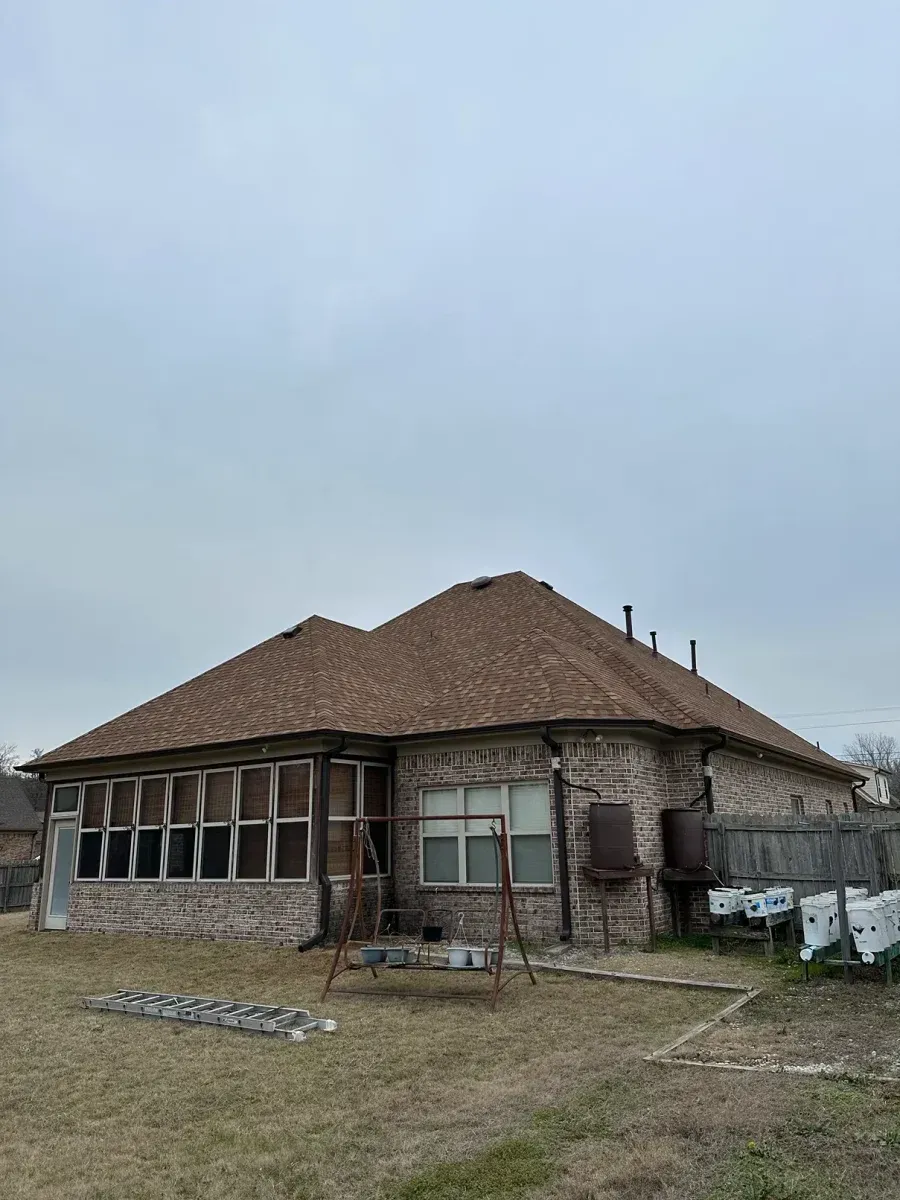 Old stone house with a brown roof, partially under construction, in a grassy field.