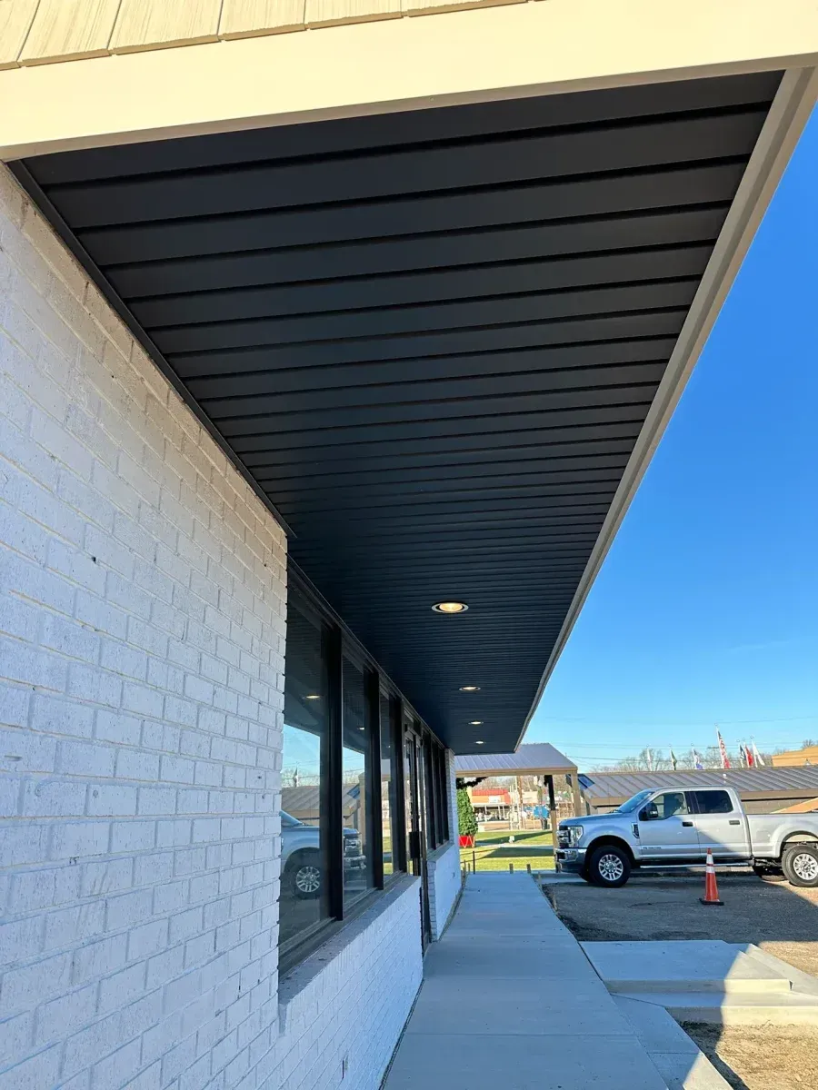 Covered storefront walkway with black soffit, white brick wall, and parked vehicles outside