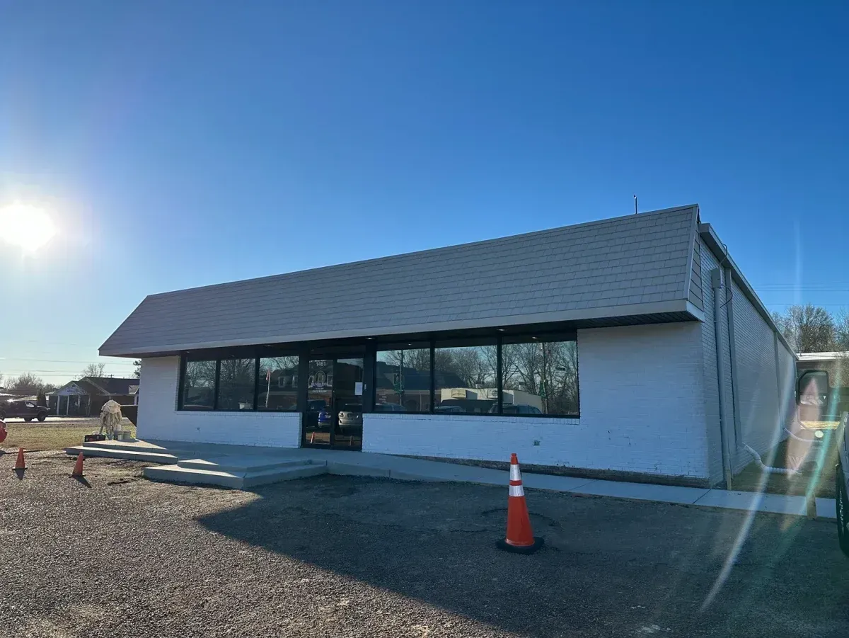 Single-story white building with dark windows, rooftop sign, and an orange traffic cone in front