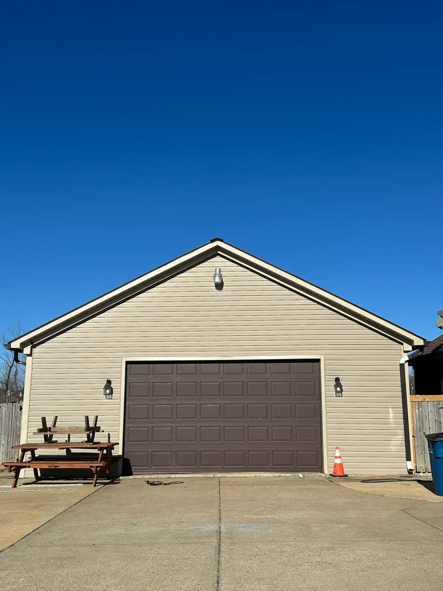 Detached beige garage with a brown door under a clear blue sky