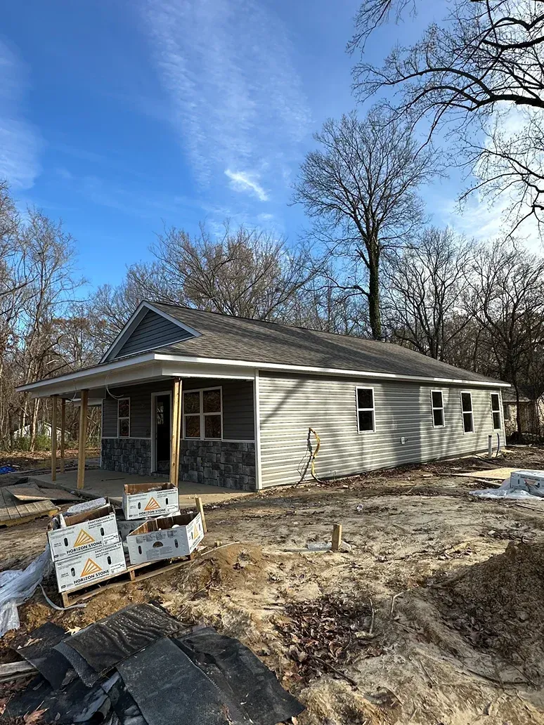 Single-story house with damaged siding and scattered debris in a snowy yard under a blue sky