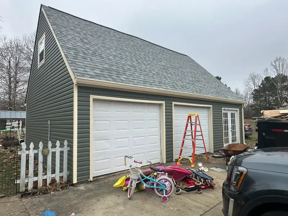 Gray garage with white doors, red ladder, and pile of colorful bikes and toys in front