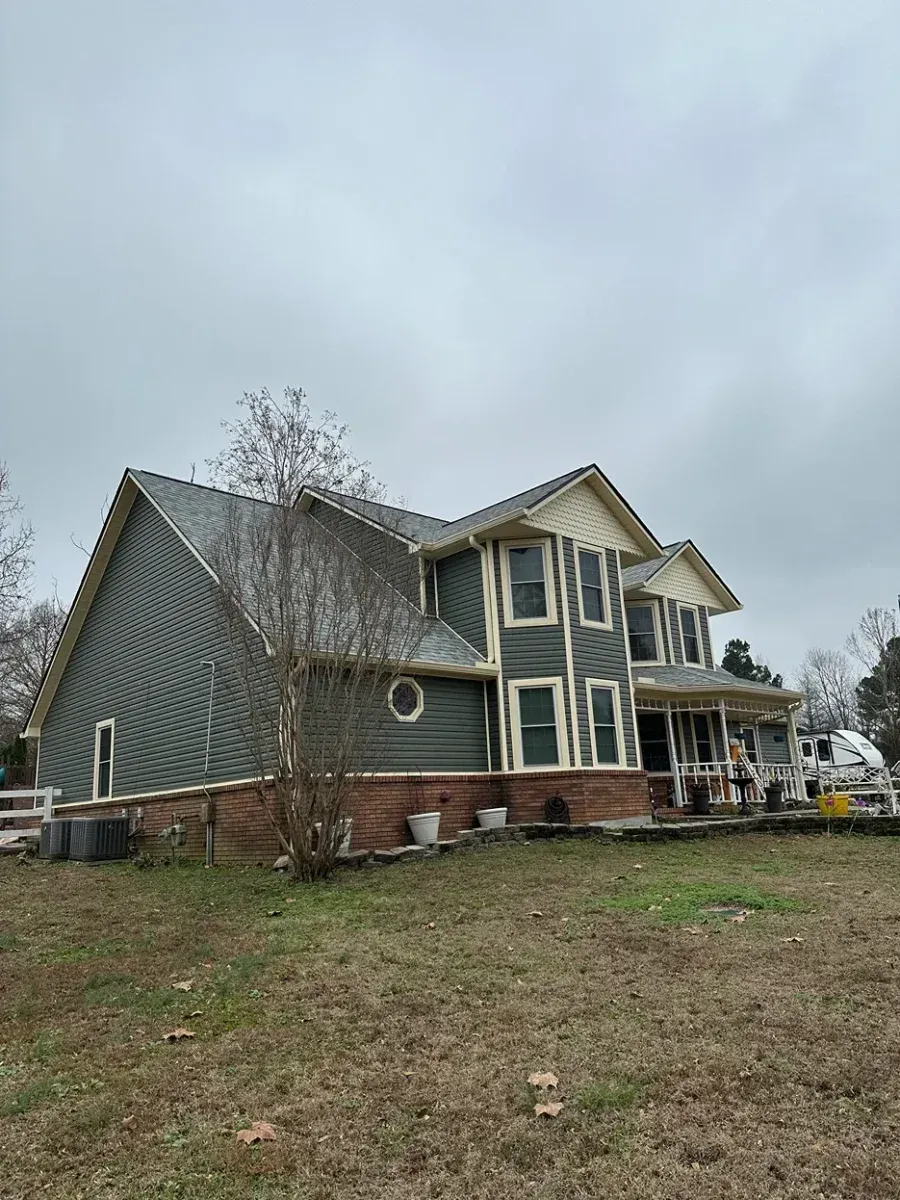 Two-story gray house with green trim on a grassy lot under an overcast sky