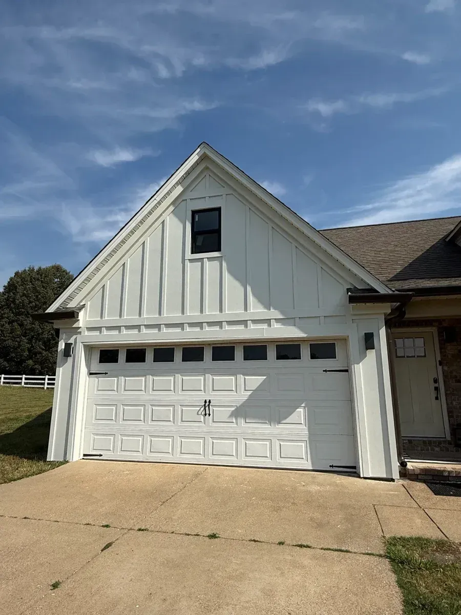 White garage exterior with a double door, dormer window, and concrete driveway under a blue sky