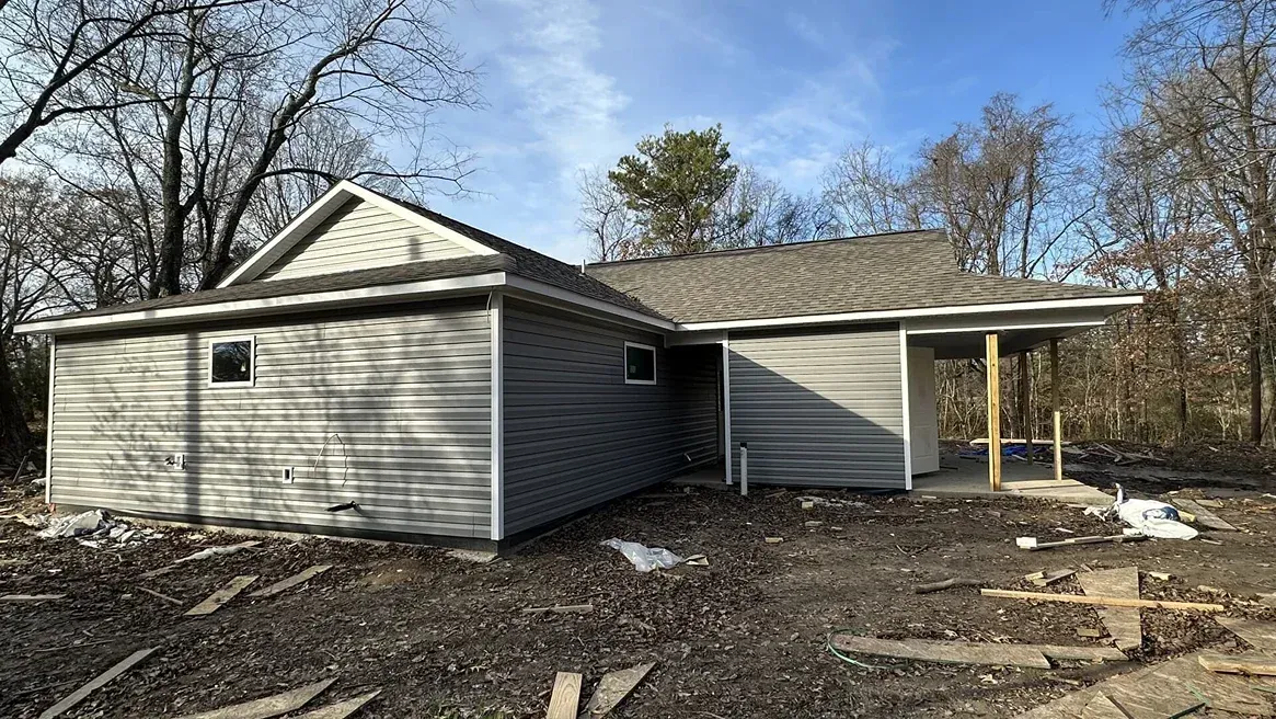 Single-story gray house with a covered porch, surrounded by bare trees and dirt yard.