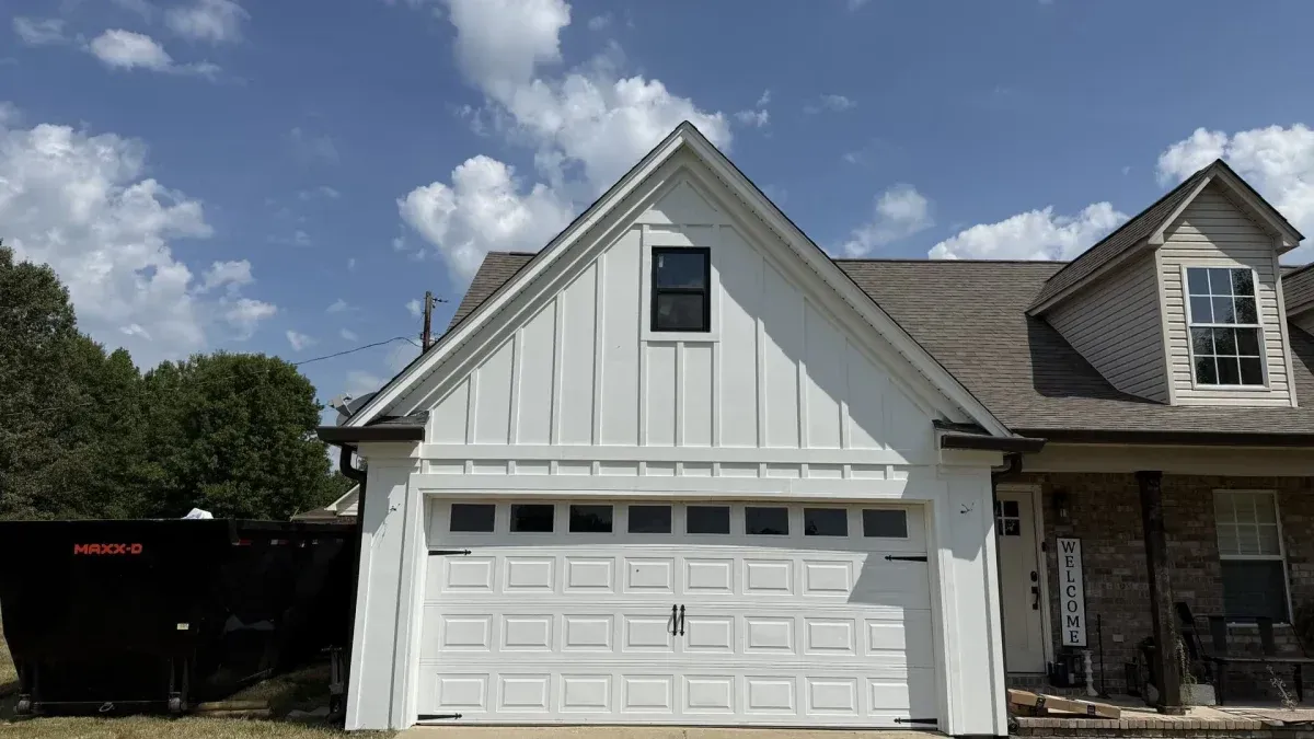 White suburban house with a two-car garage, stone siding, and dormer windows under a partly cloudy sky