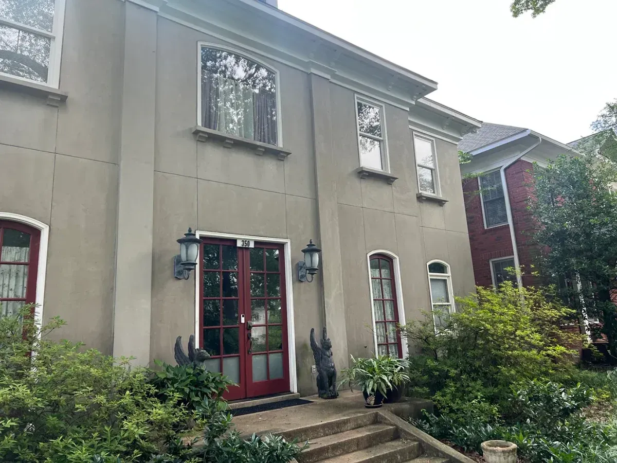 Gray two-story house with red front door, arched windows, and lush garden greenery