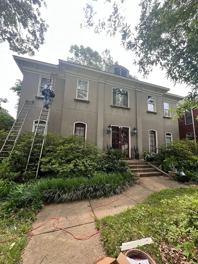 Two-story gray house with a worker on a ladder trimming trees in the front yard