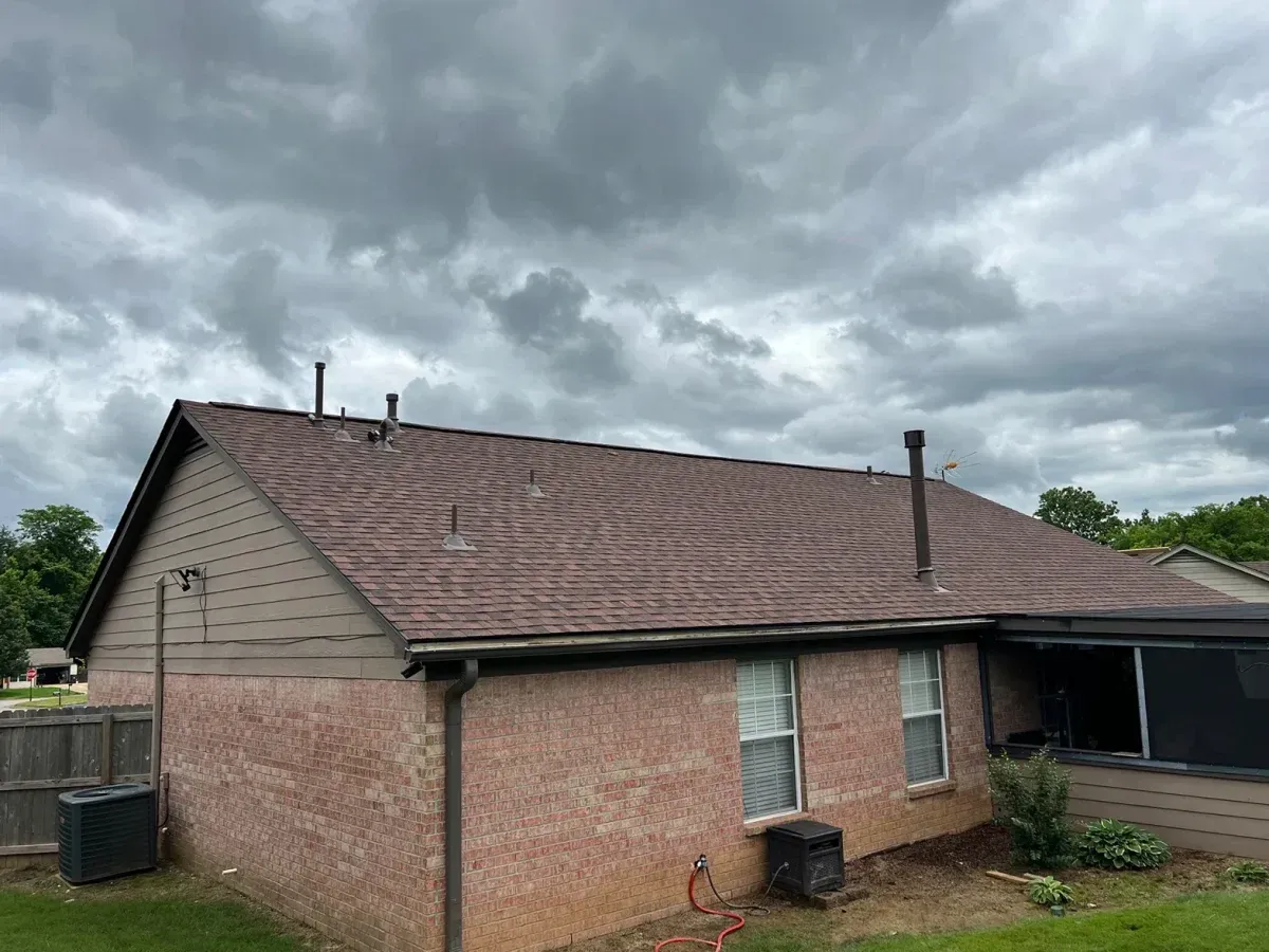 Brick house with a brown roof under cloudy skies, with a small covered patio on the right.