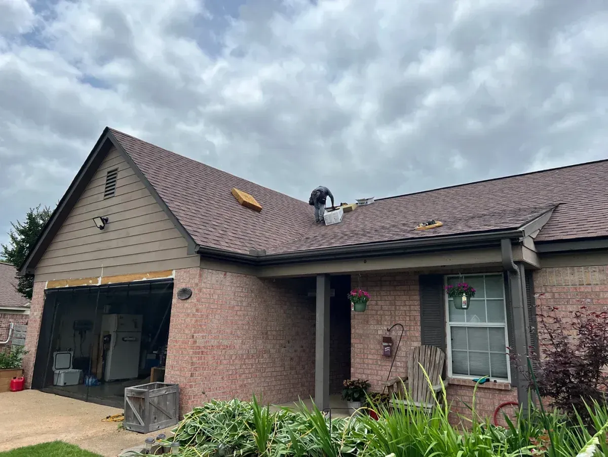 Brick house with damaged shingled roof and an open garage under cloudy skies