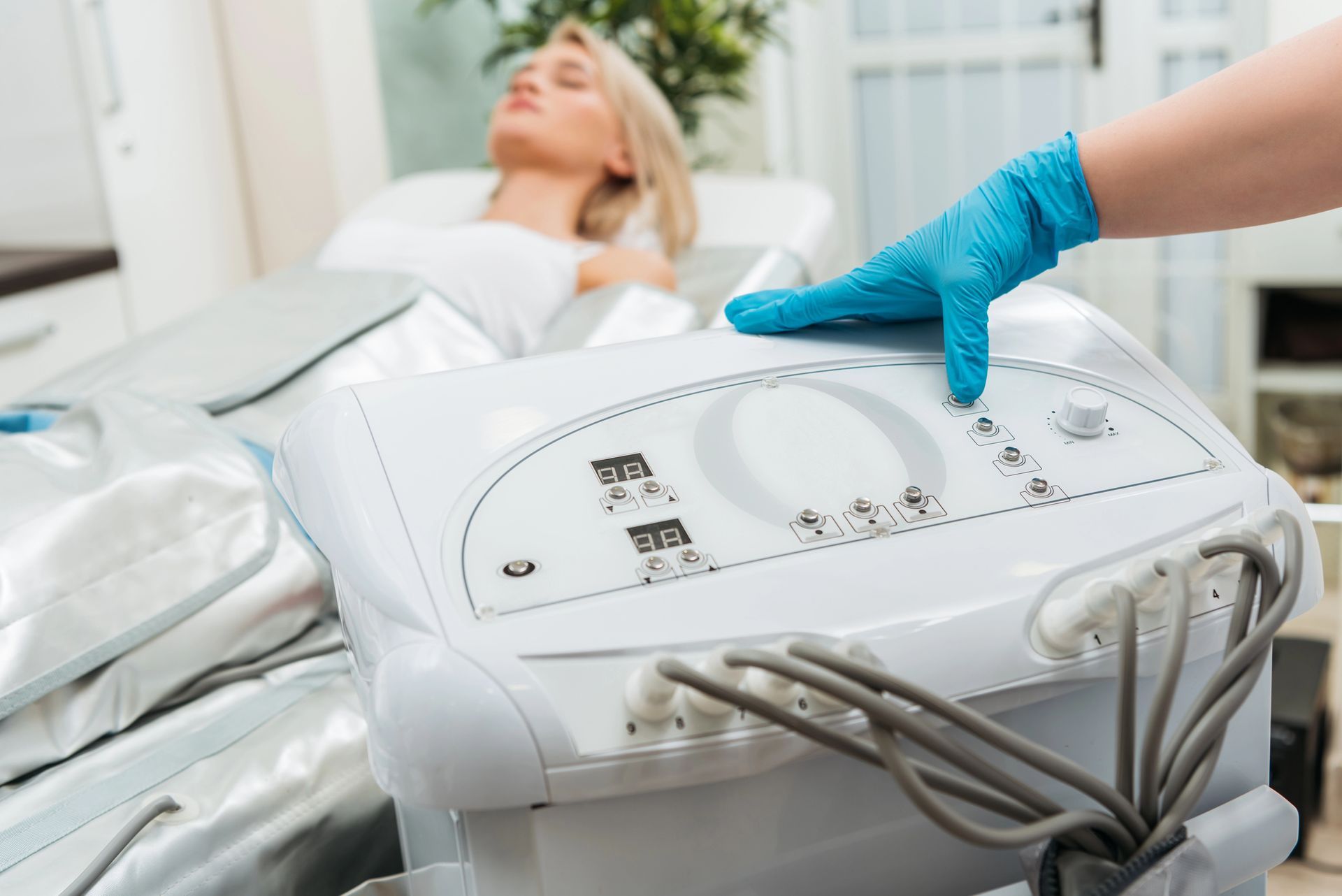 Una mano guantata utilizza un dispositivo per trattamenti viso accanto a una cliente sdraiata su un lettino da spa.