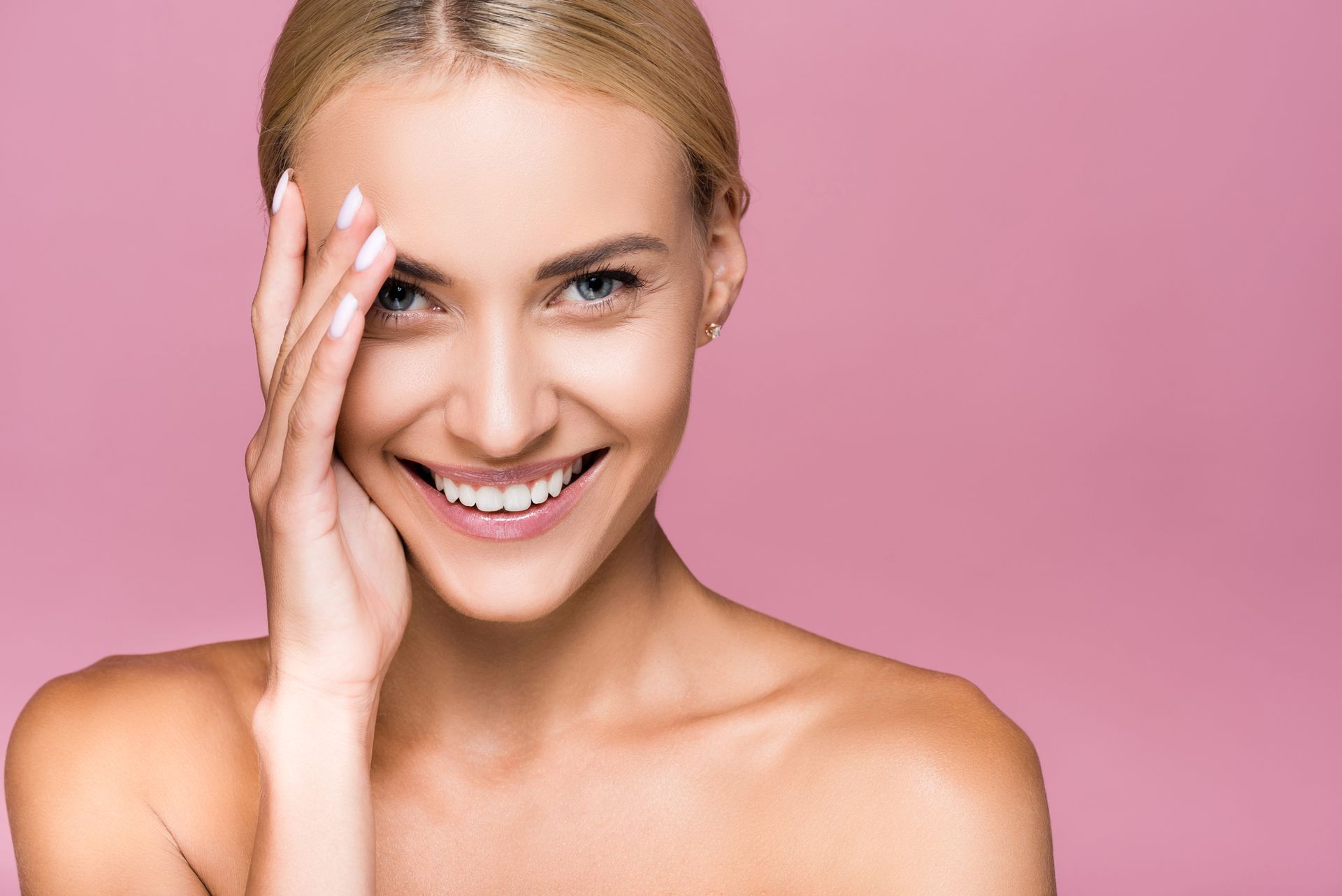 Donna bionda sorridente su sfondo rosa, si tocca il viso