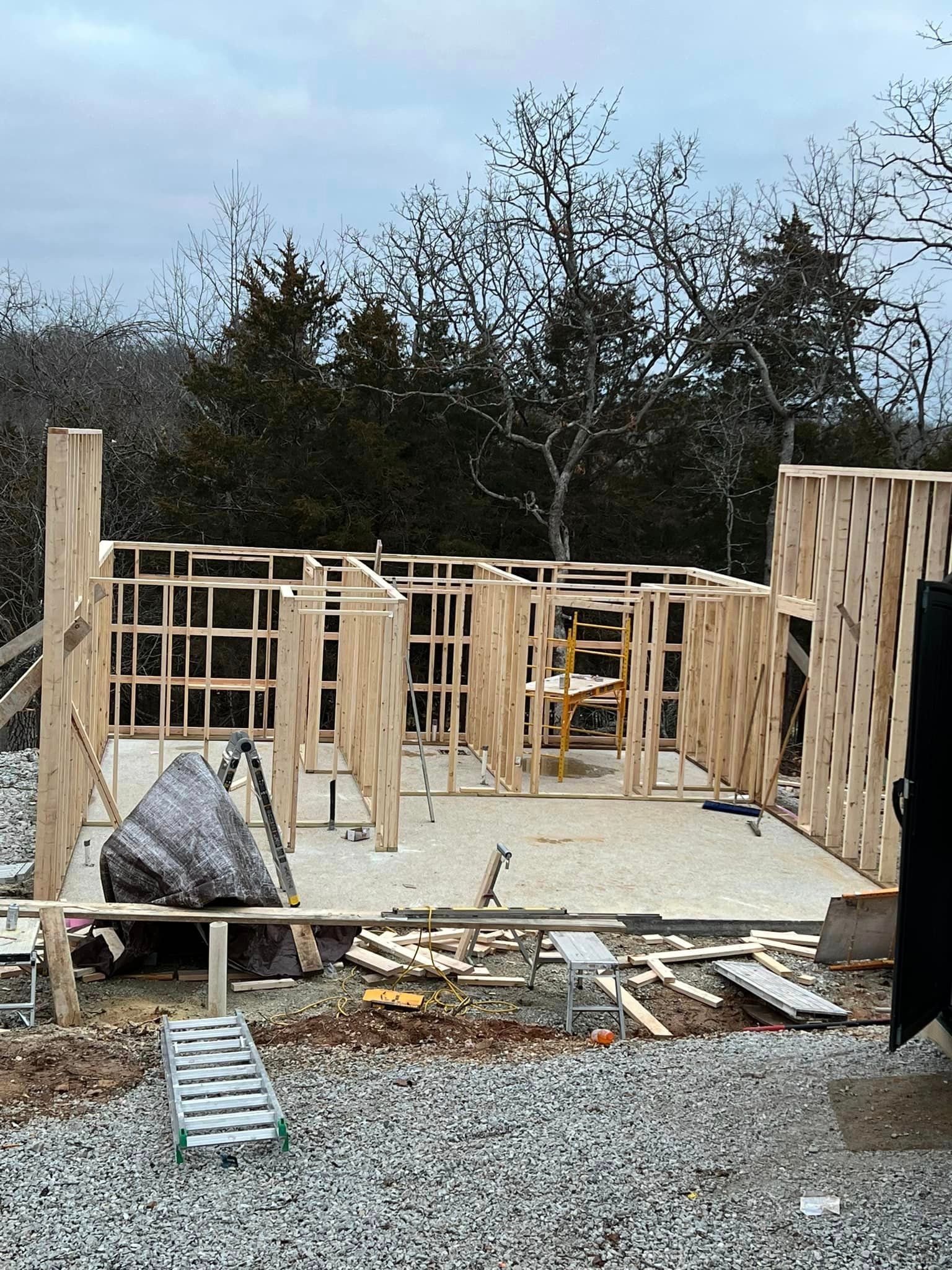 A house is being built on a gravel lot in the woods.