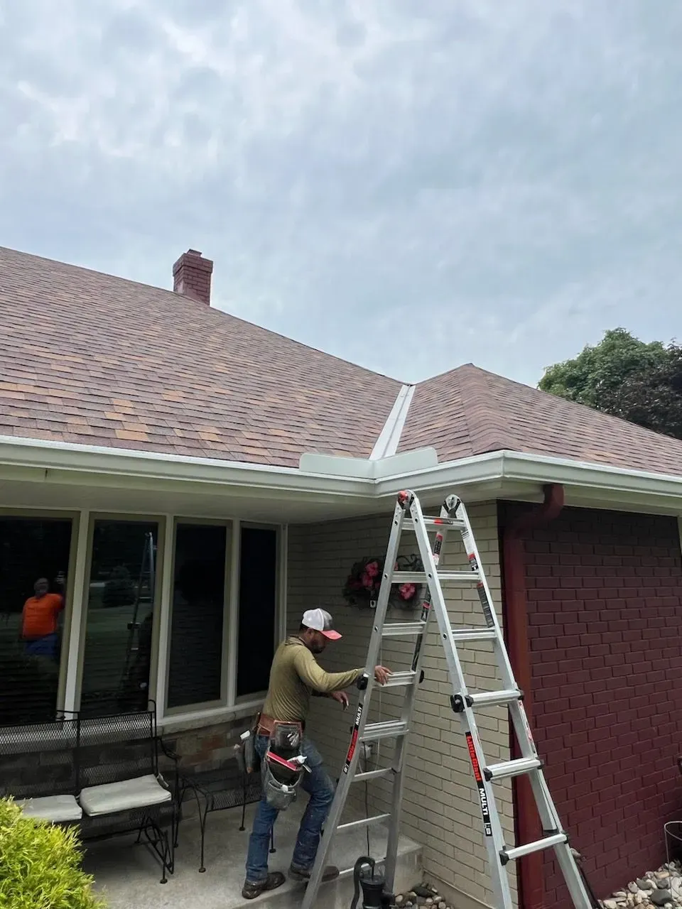 A man is standing on a ladder on the side of a house.