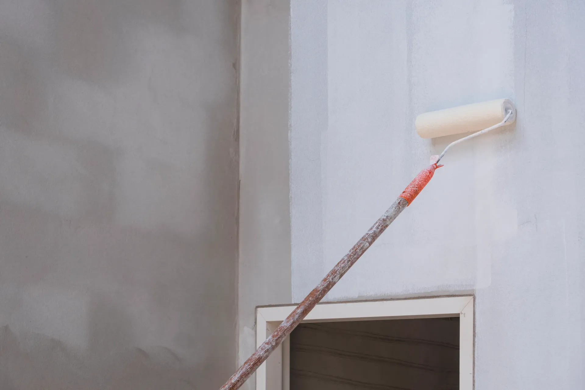 A person is painting a wall with a paint roller.