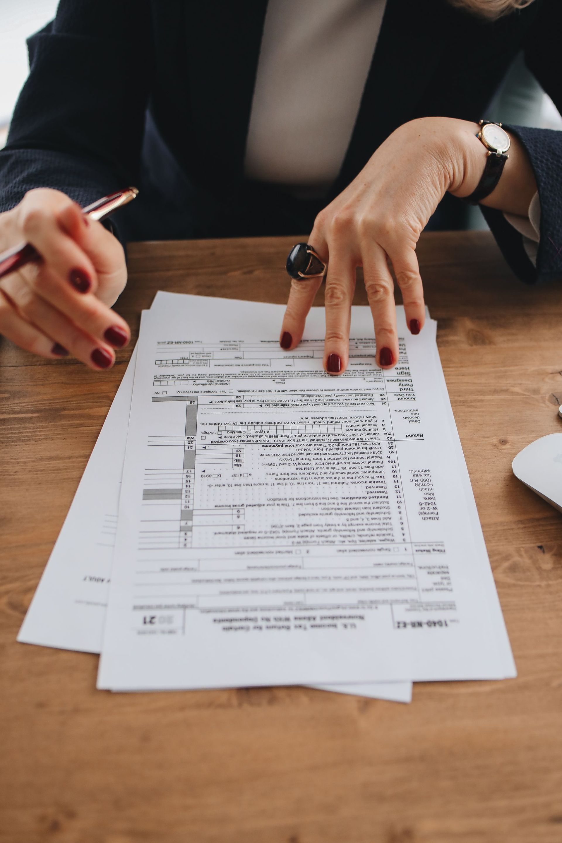 Hands reviewing a document on a wooden table, one person pointing with a pen and another wearing a watch.