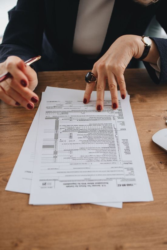 Two hands reviewing and signing documents on a wooden table with a pen and wristwatch