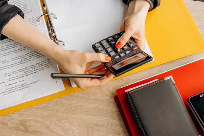 Hands using a calculator and pencil over paperwork on a desk with notebooks and folders