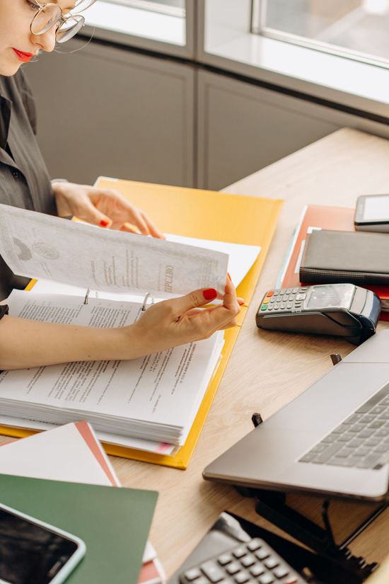 Person reviewing documents at a desk with a laptop, notebook, and phone in a bright office space