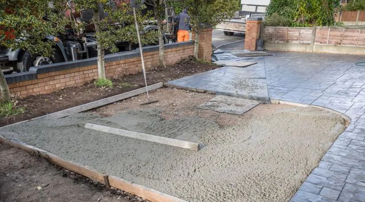 Partially finished concrete driveway with wooden forms and stone pavers beside a garden wall