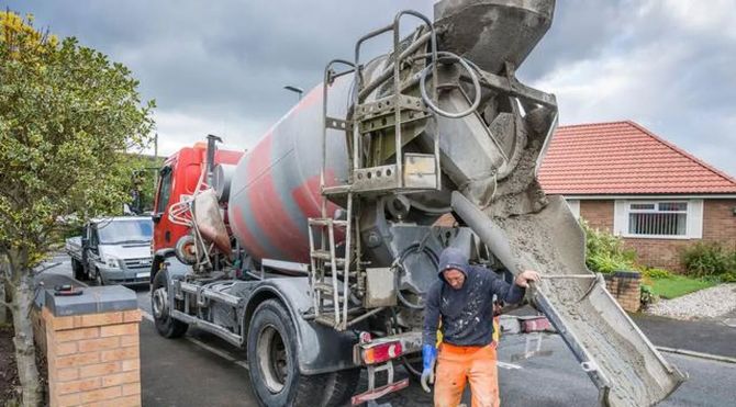 Concrete mixer truck unloading on a residential street, with a worker guiding the chute