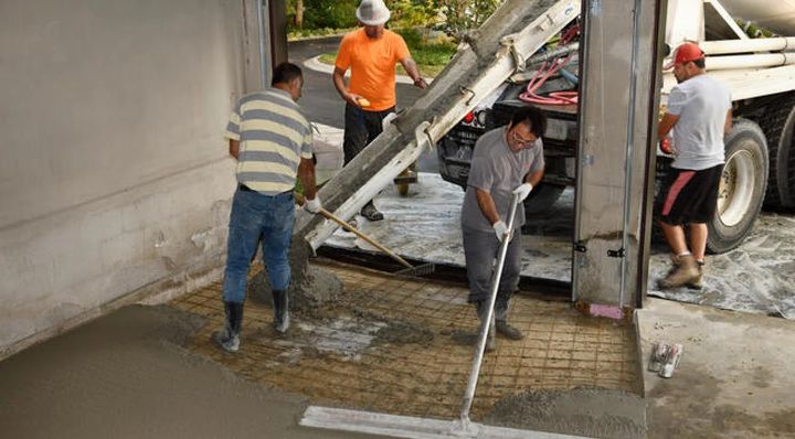 Workers in safety gear pouring and leveling concrete in a construction area