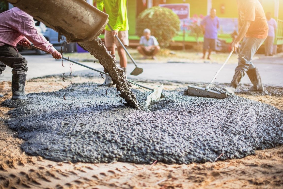 Workers pouring wet concrete onto a construction site at sunrise