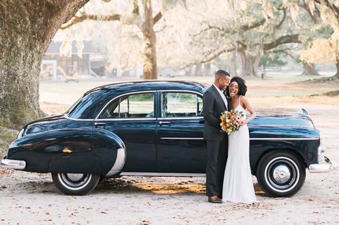 A bride and groom are posing for a picture in front of an old car.