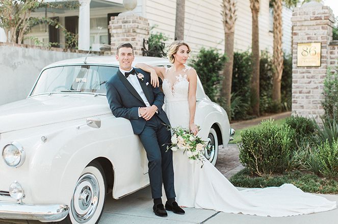 A bride and groom are posing for a picture next to a white car.