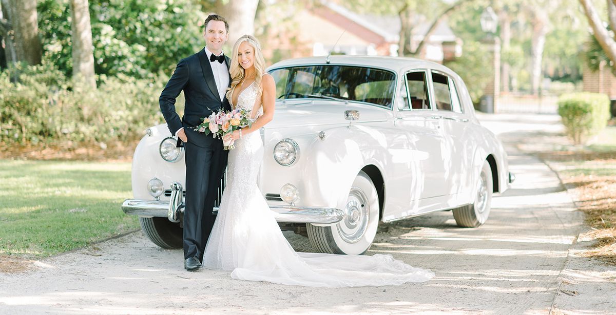 A bride and groom are posing for a picture in front of a white car.