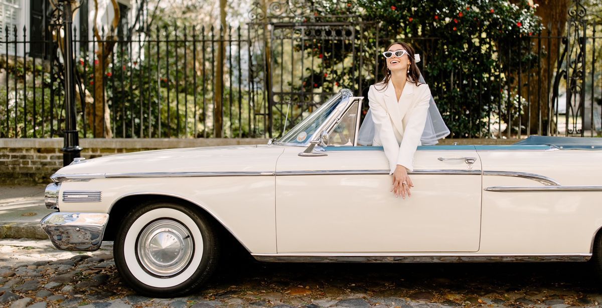 A woman is sitting on the side of a white convertible car.
