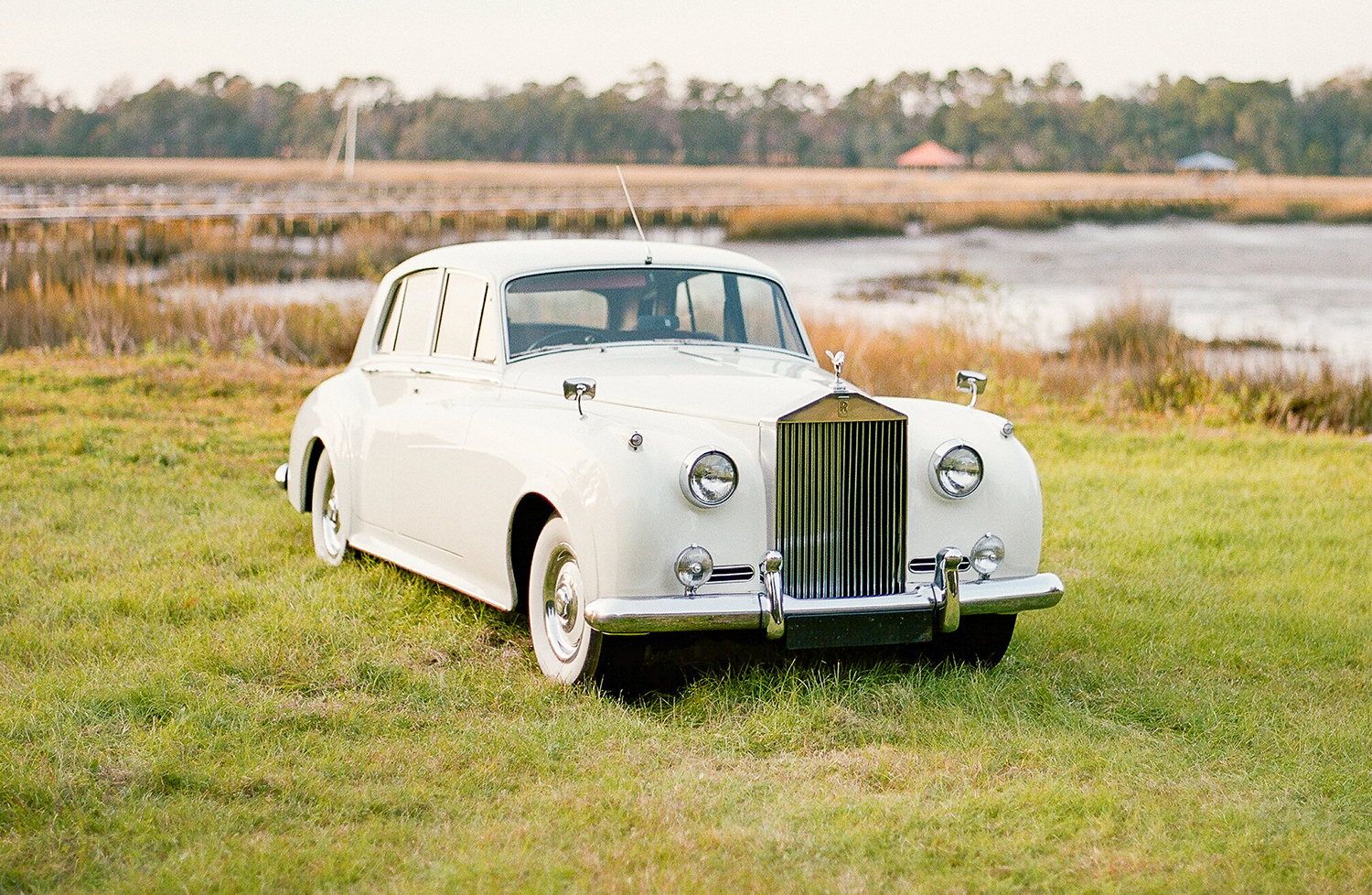 A white rolls royce is parked in a grassy field.