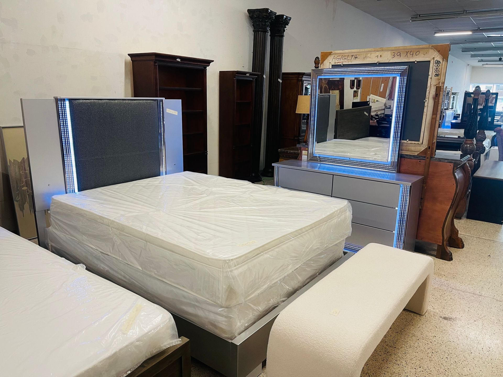 A showroom display of a bedroom set with a grey upholstered headboard and dresser featuring blue LED lighting.