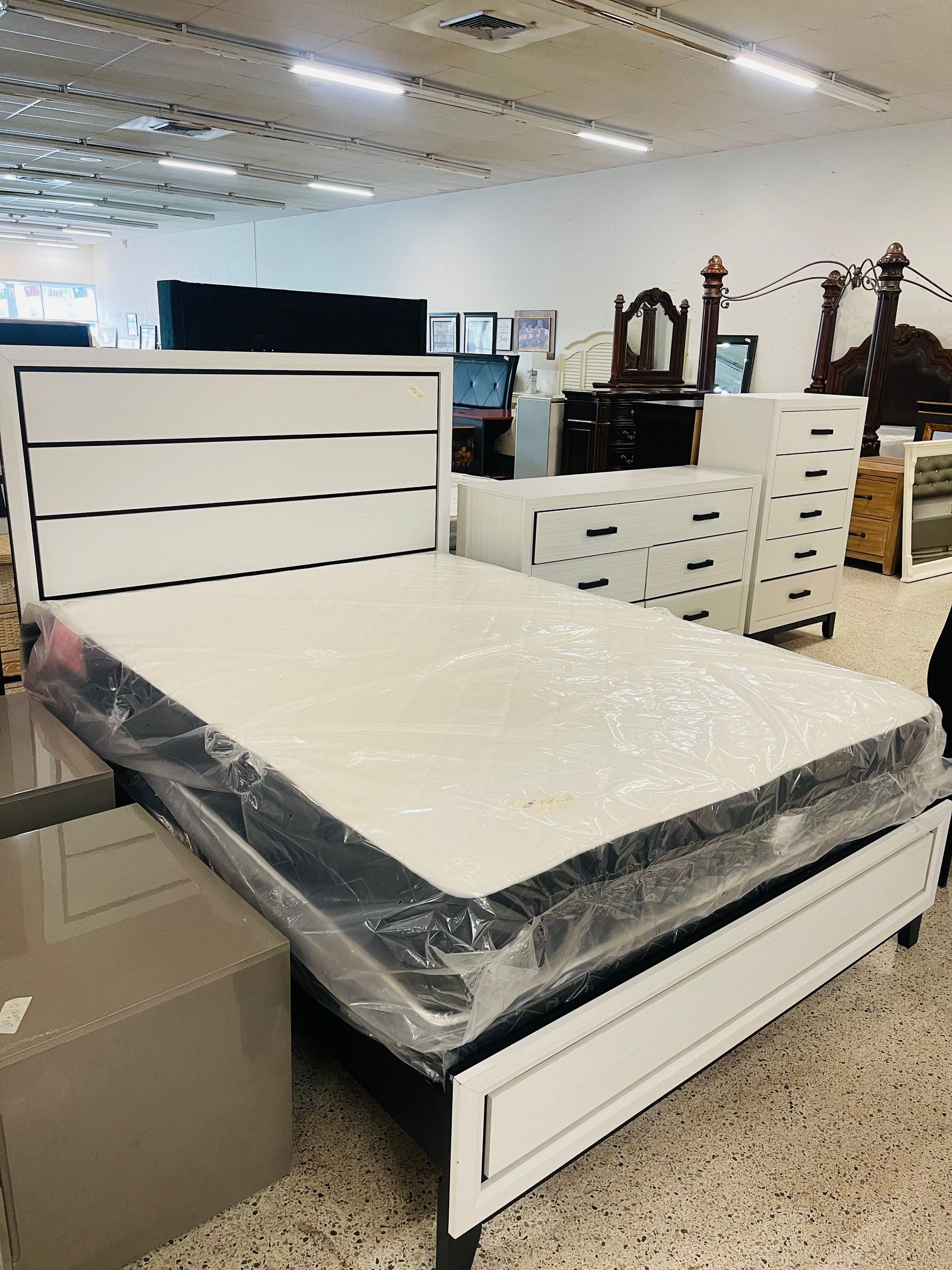 A modern white bed frame with a paneled headboard and mattress in a brightly lit furniture showroom.