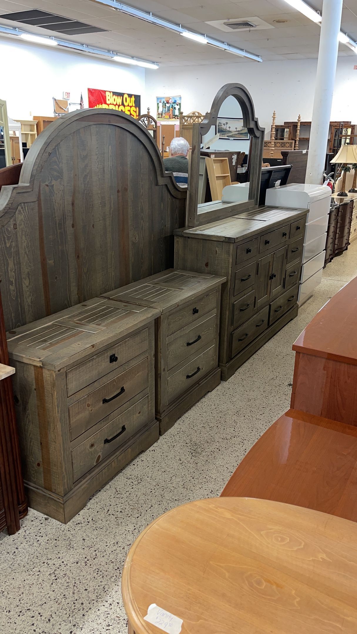 A rustic gray wooden dresser and matching mirror in a furniture store, set against a backdrop of other items for sale.