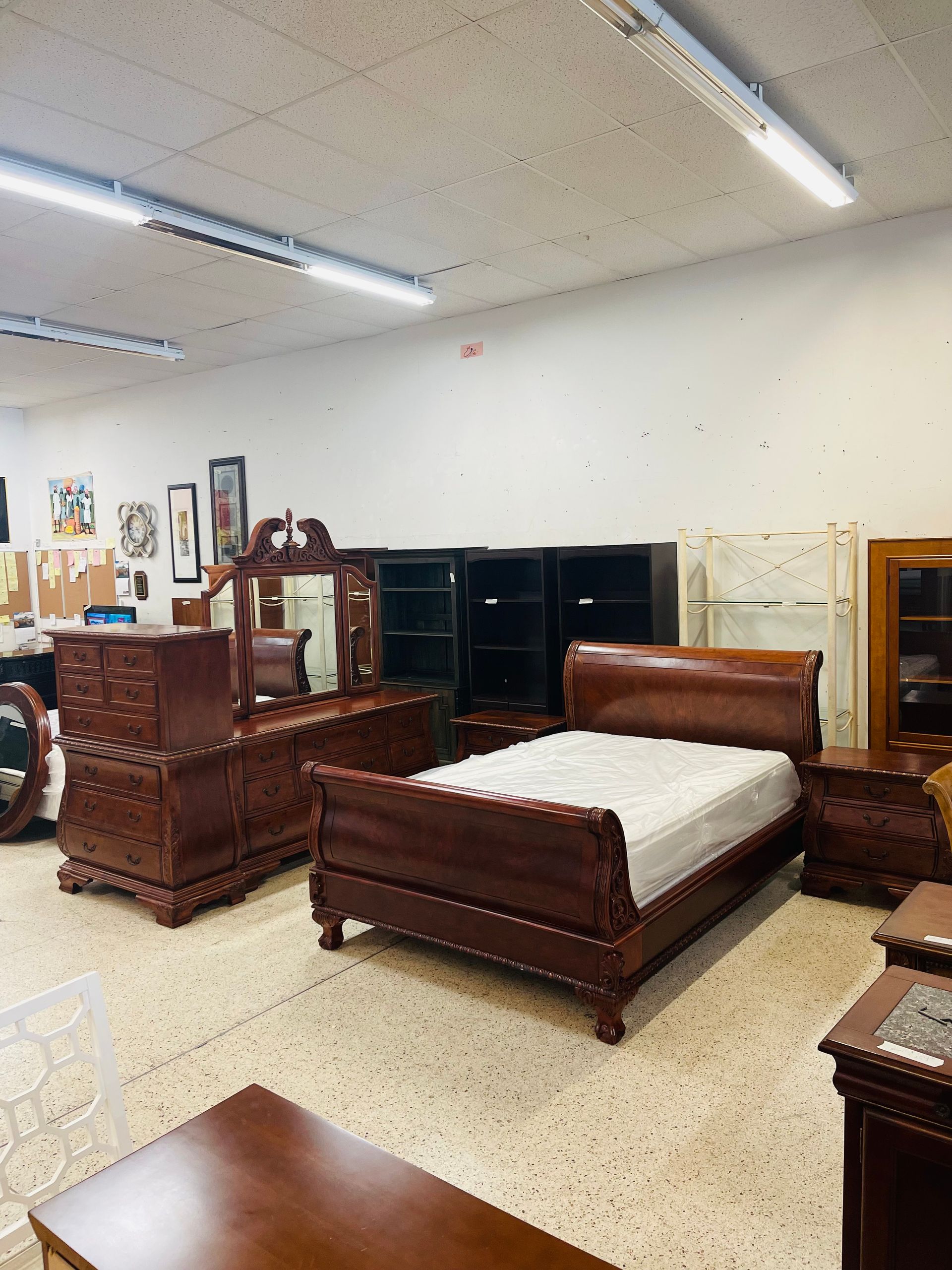 A showroom display featuring a dark wood sleigh bed, a matching dresser with a mirror, and a nightstand.