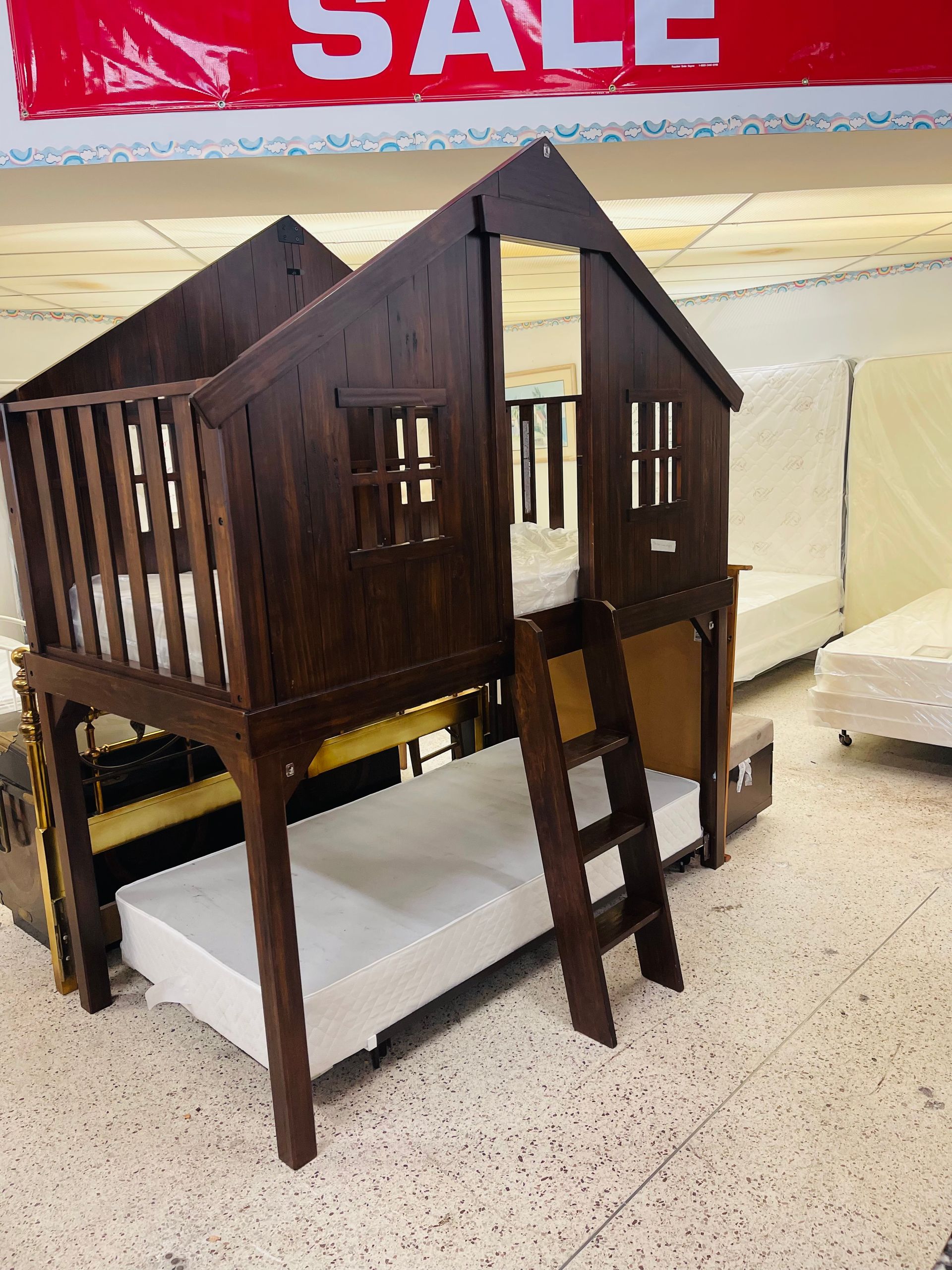 A dark wood treehouse-style bunk bed with a ladder, shown in a store furniture display.