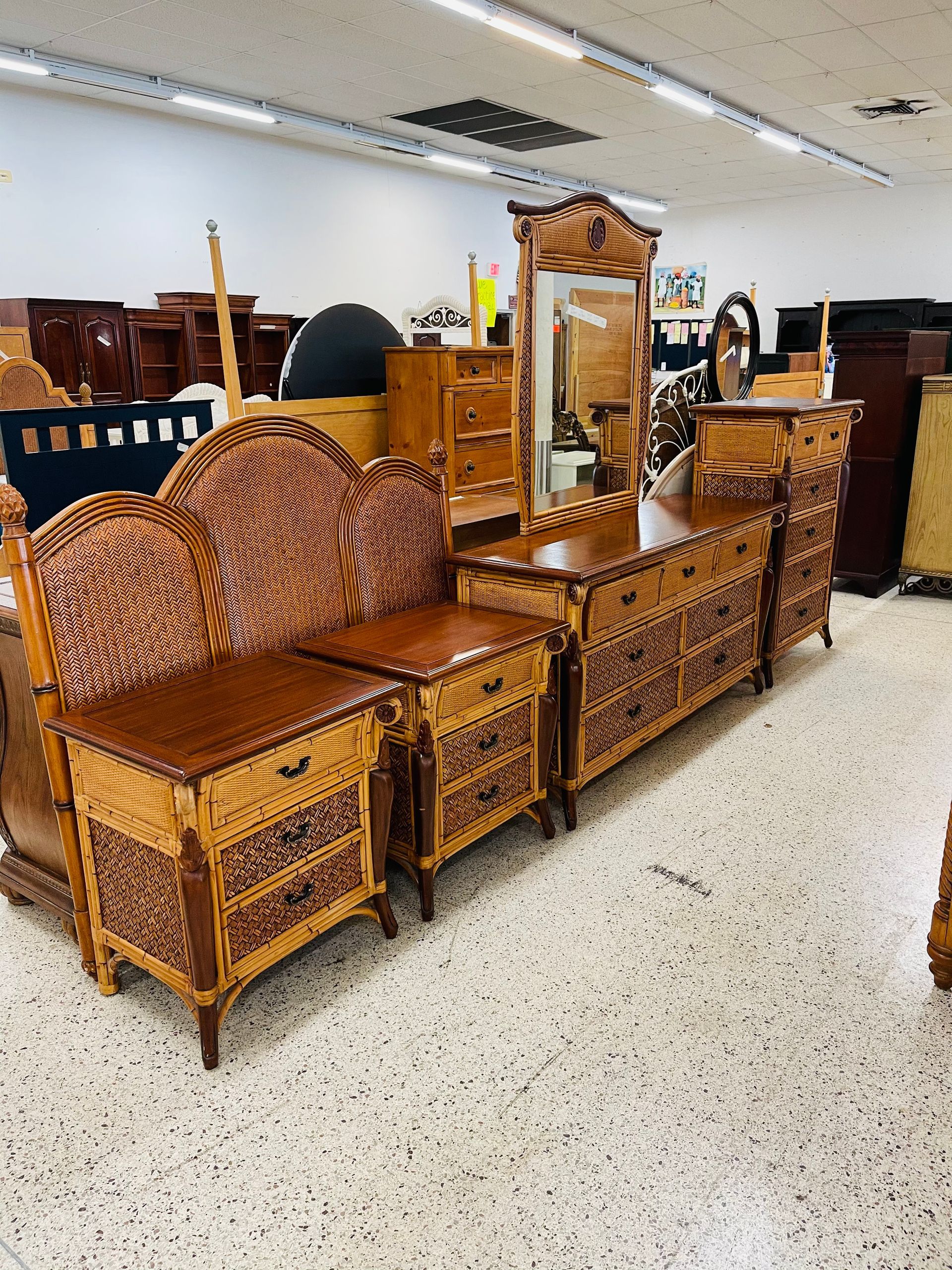 A bedroom furniture set featuring woven wicker and dark wood, displayed in a bright retail store with speckled flooring.
