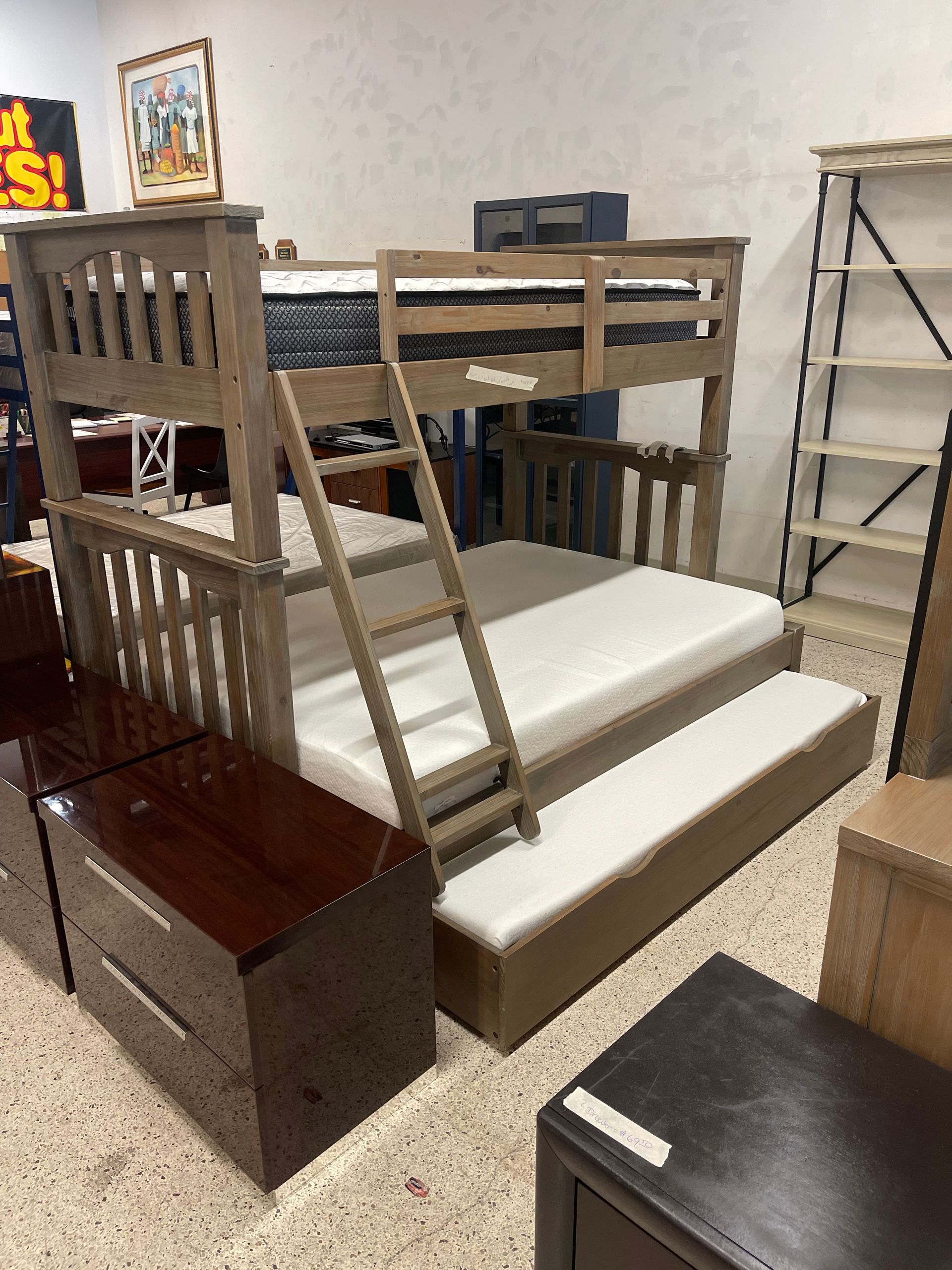 A wooden bunk bed with a trundle mattress in a furniture showroom.